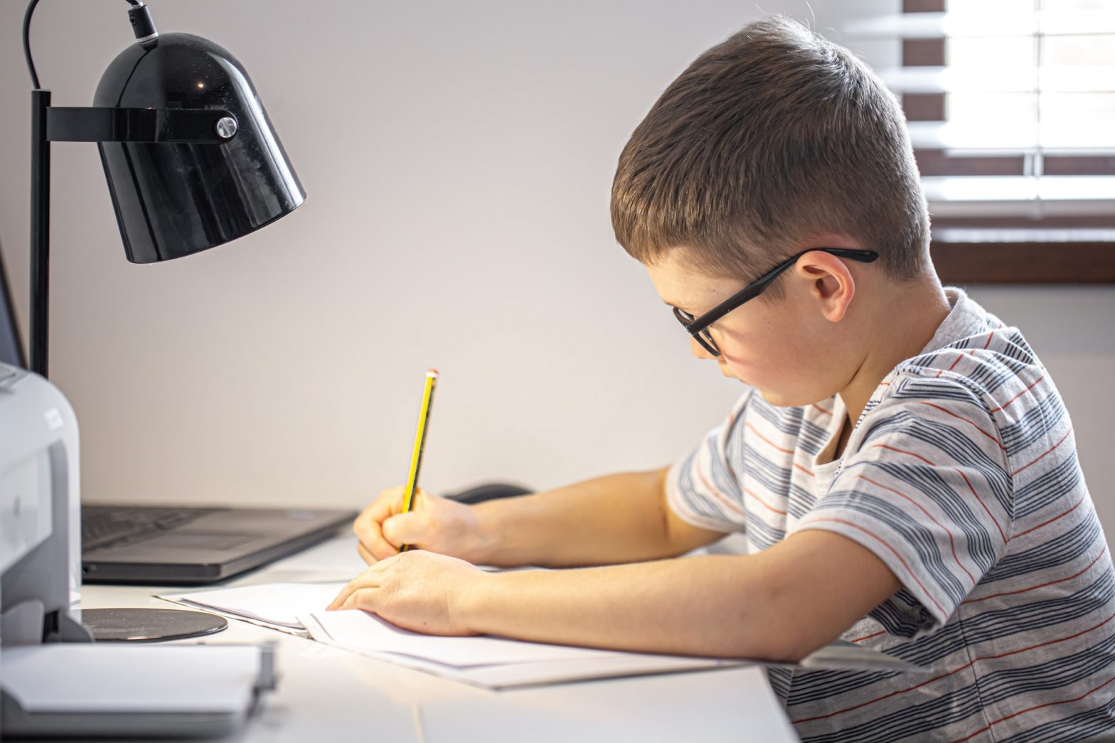 Little boy in glasses does homework sitting at the desk.