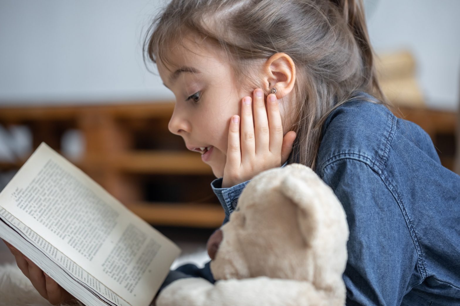 Little girl reads a book with a teddy bear.