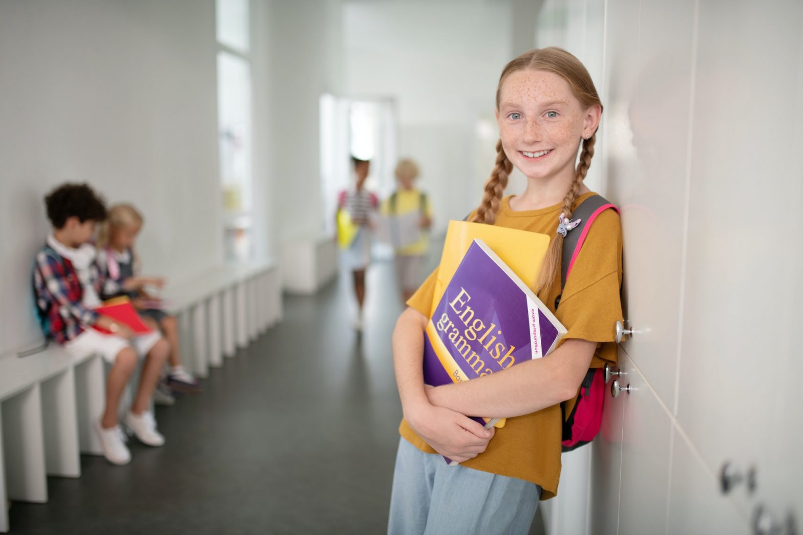 Beautiful schoolgirl holding boy while standing near locker