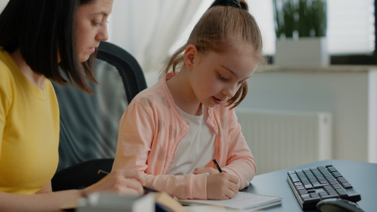 Young child writing homework on notebook and mother assisting