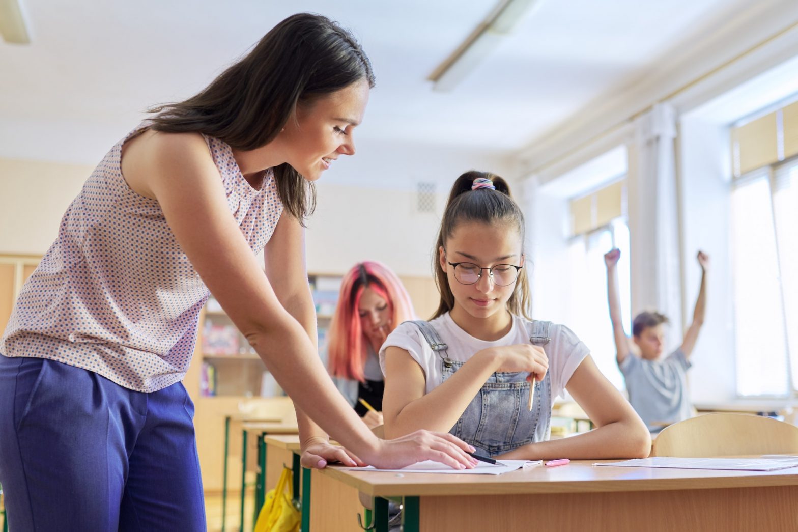 Young woman teacher teaches lesson in class of teenage children