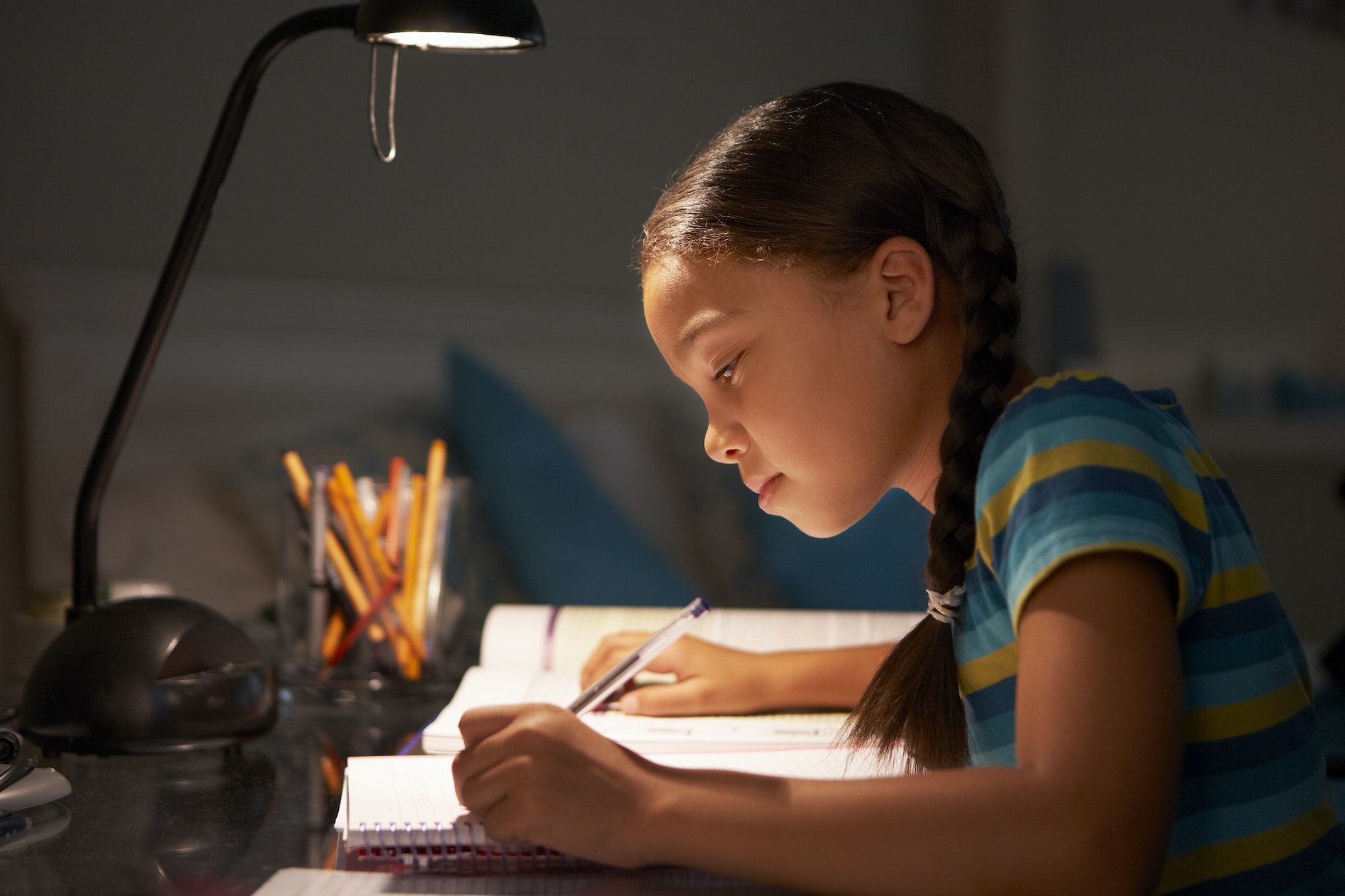 Young Girl Studying At Desk In Bedroom In Evening